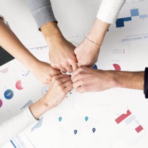Colleagues celebrate success with a fist bump over financial charts depicting teamwork and unity.